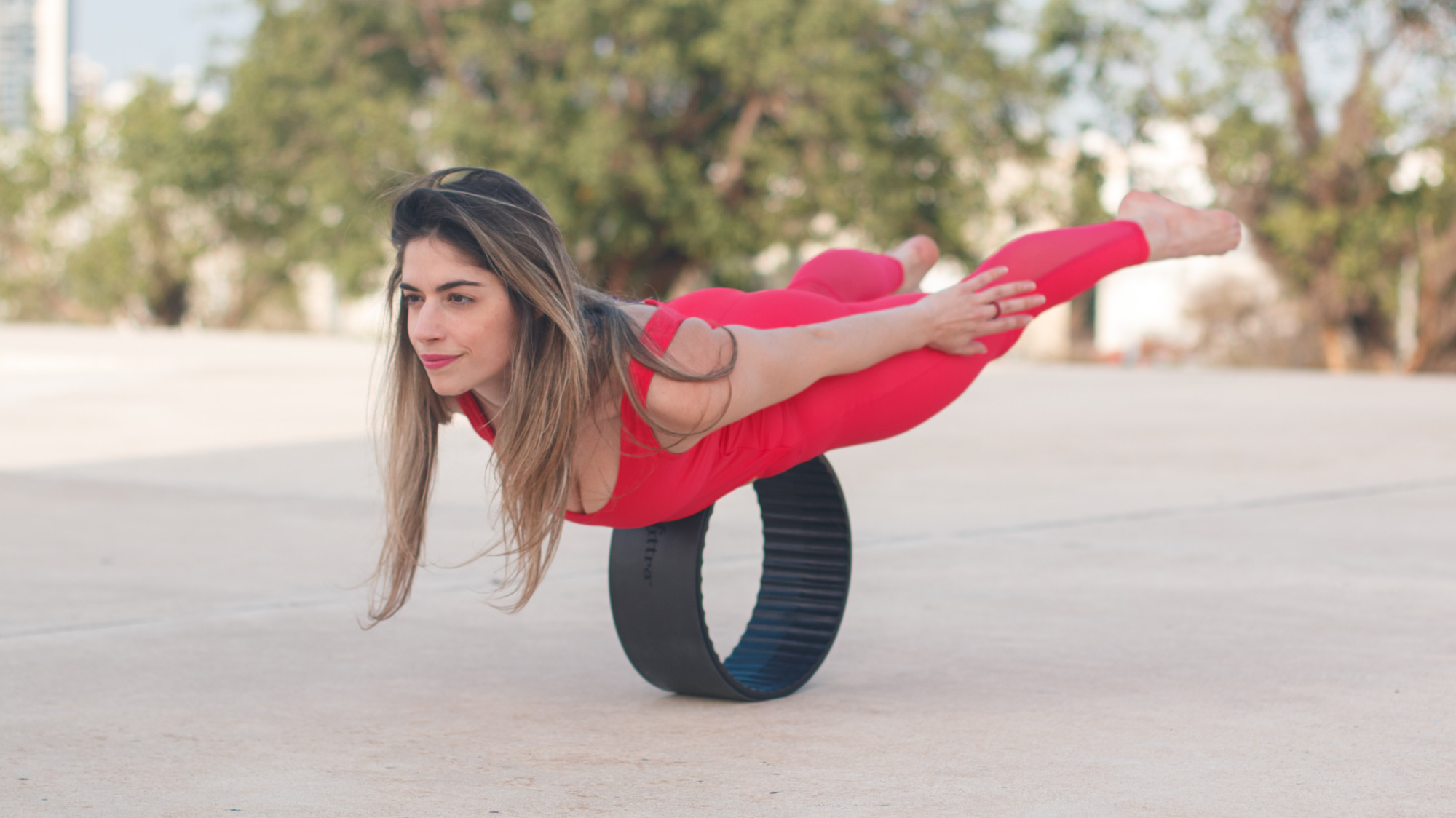 A woman in exercise wear planks on her belly on a pilates ring. She is outside.