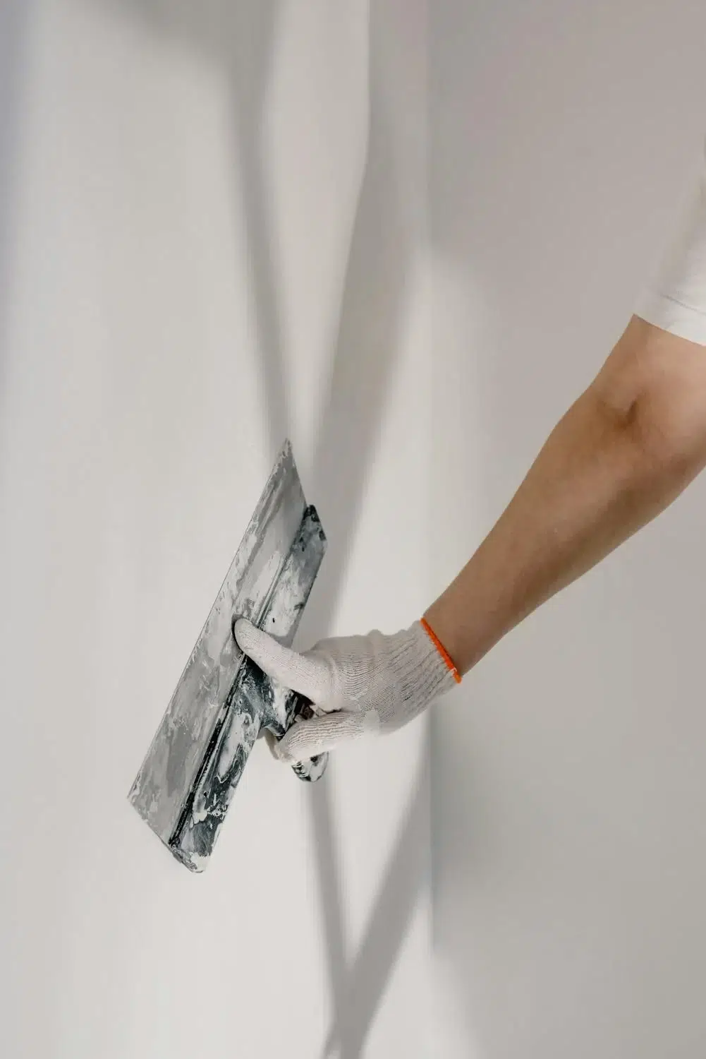 A hand wearing a protective glove plasters a wall