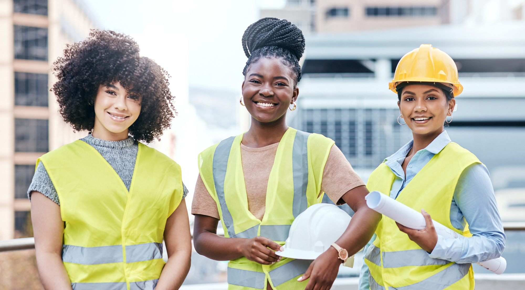 Three women smiling directly at camera working on a construction site