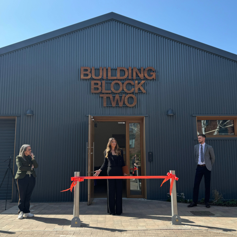A clear blue sky, and three colleagues talk to the crowd before they cut the orange ribbon to declare it open