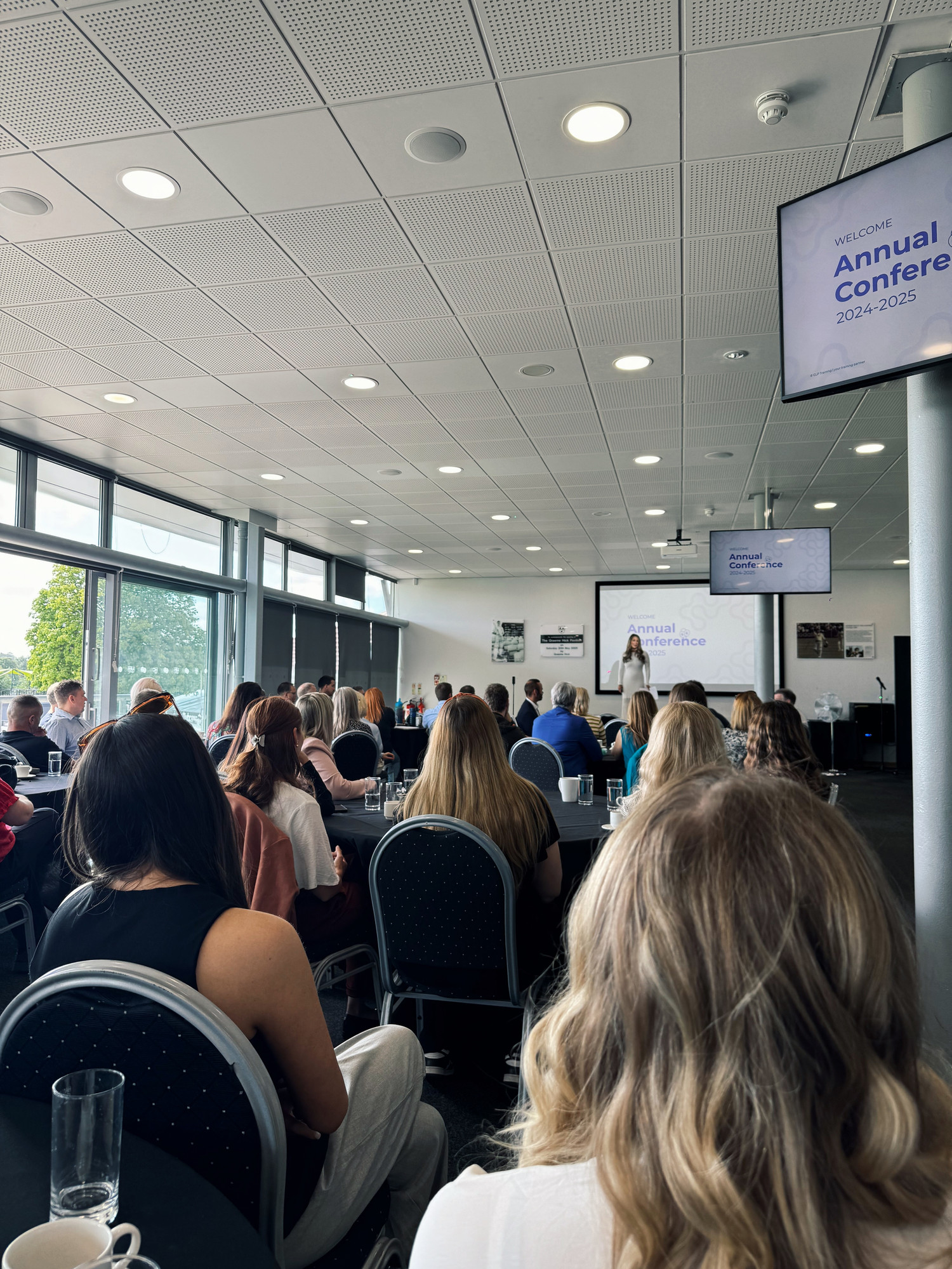 GLP Training's Annual Conference. A woman addresses the room from the stage.