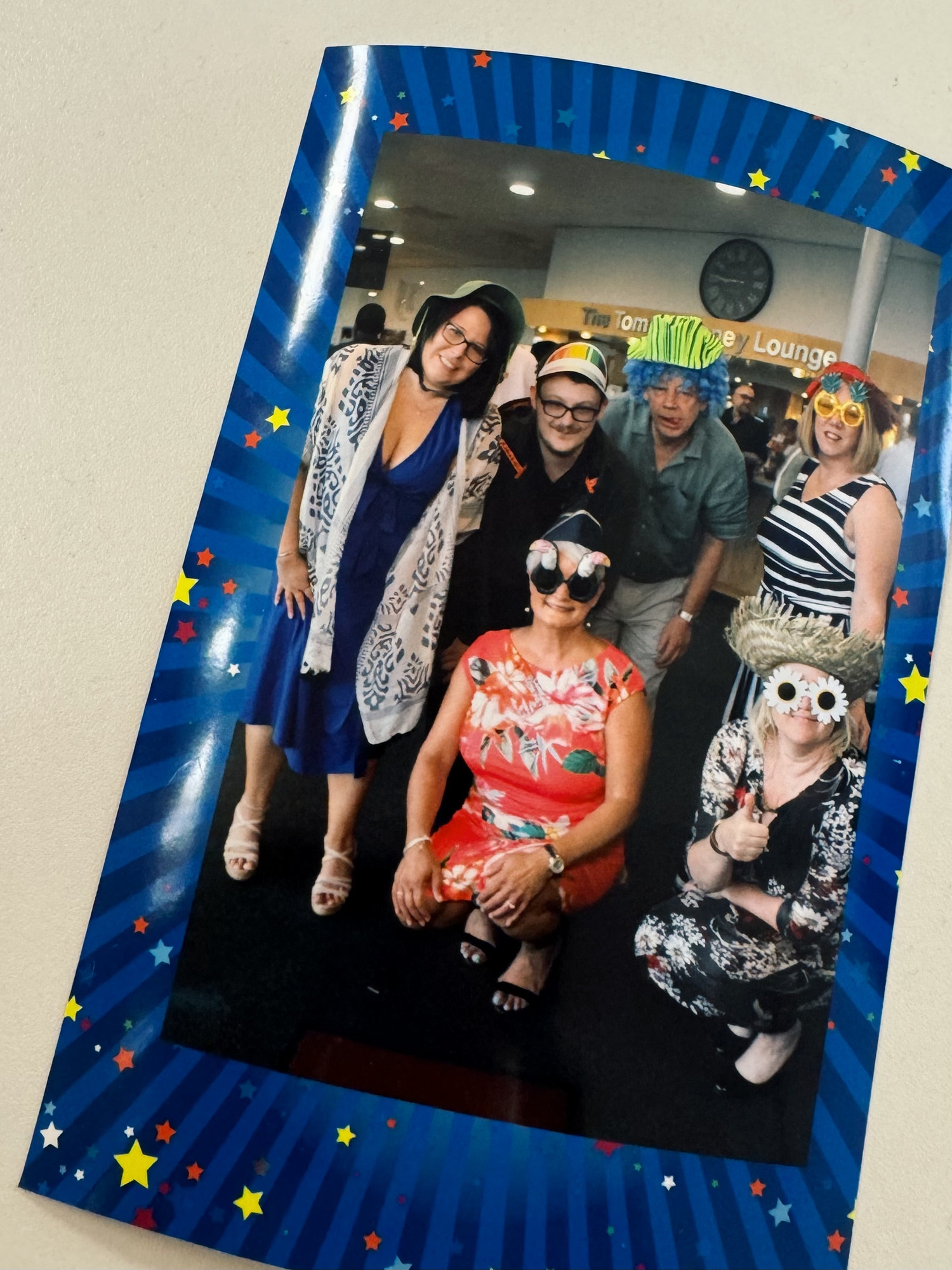 A group of people in formal wear wearing fun hats and glasses and wigs pose for the camera.