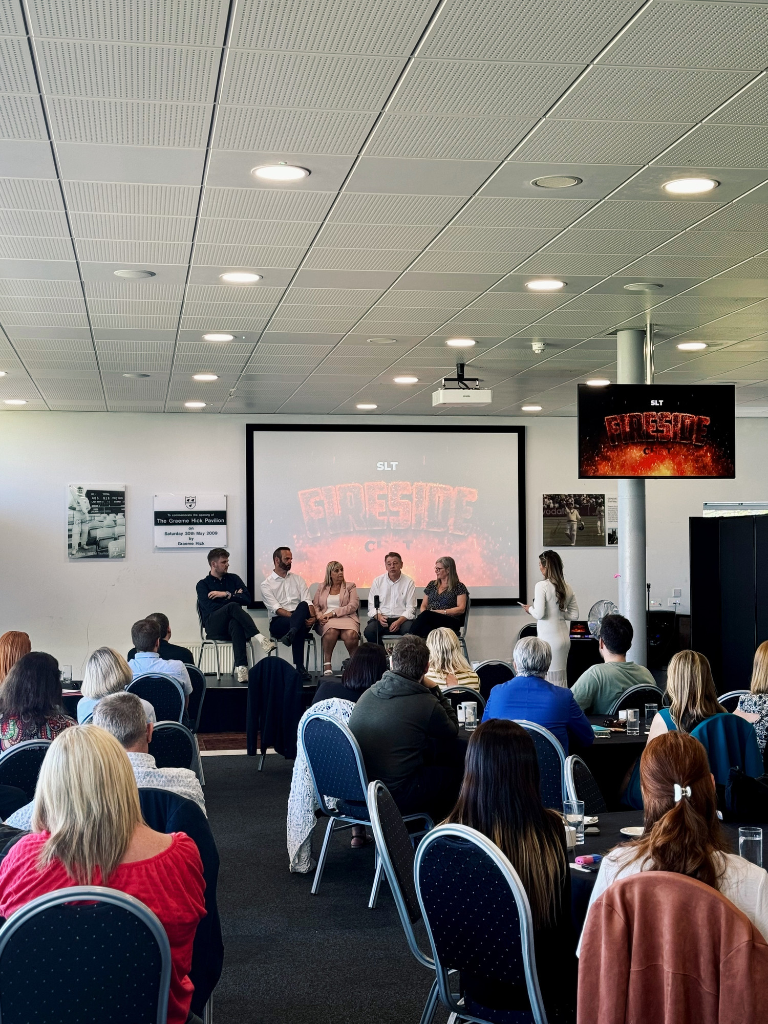 5 people talk at a conference to a room of people. On the screen reads 'FireSide'