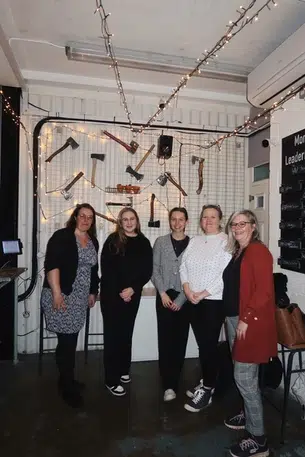 5 women in smart casual wear pose for the camera at an axe throwing centre.