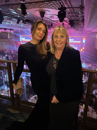 Two women in formal wear smile and pose together for the camera at an award's ceremony