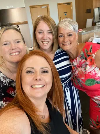 4 women in formal wear take a selfie - they all smile