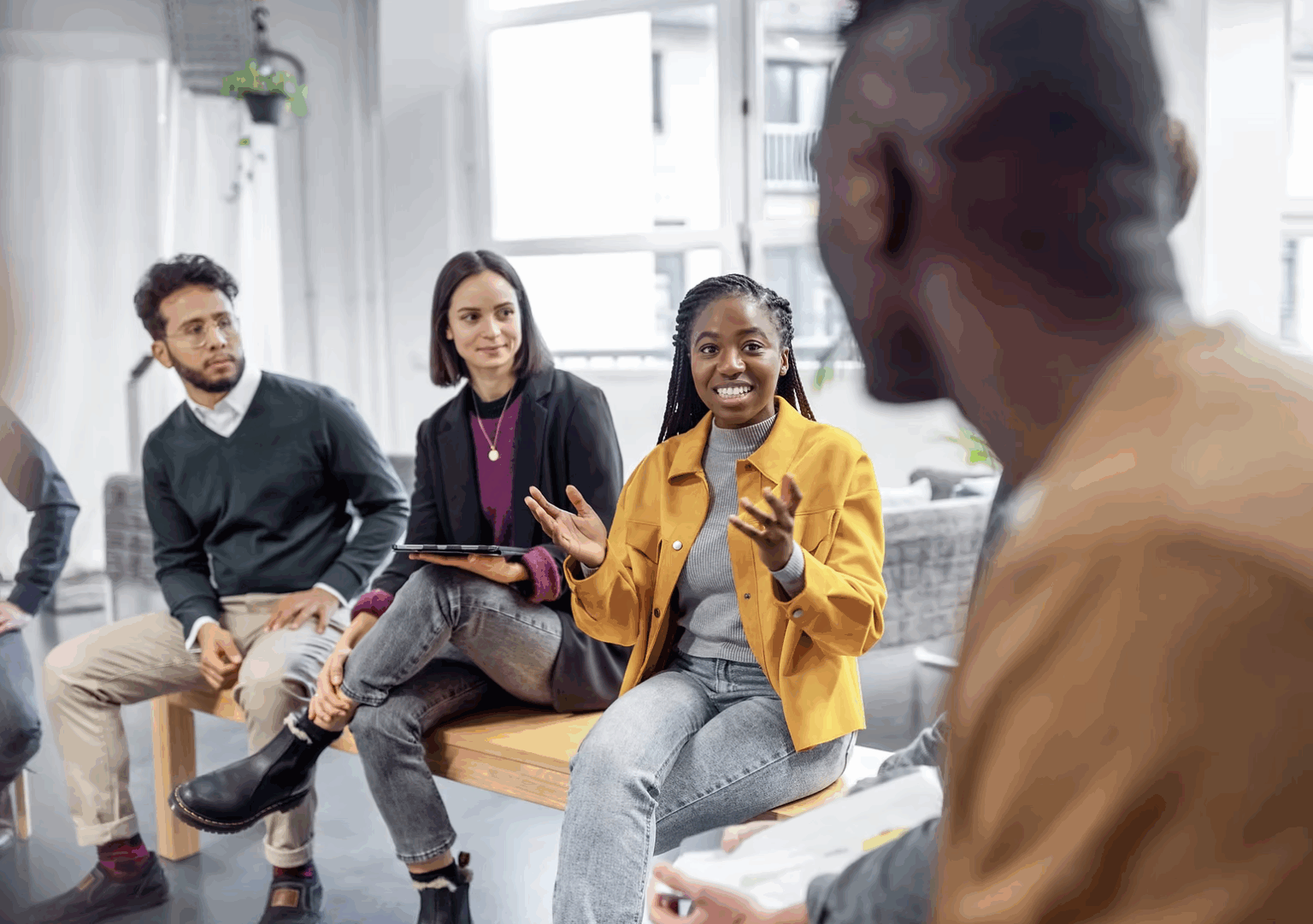 A diverse group of 4 students have an animated conversation together in a brightly lit class room