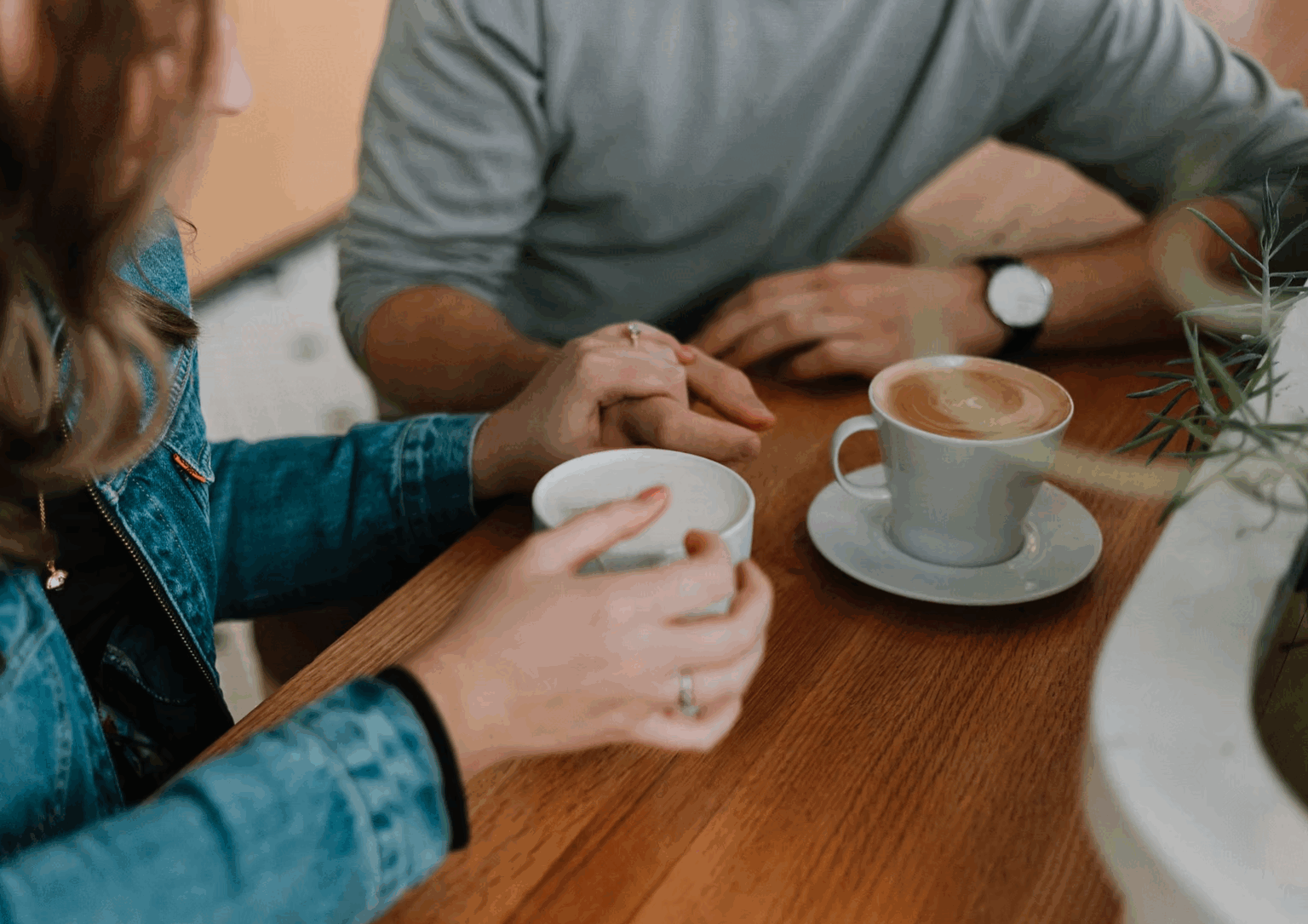 A female hand grasps a male hand over two cups of coffee