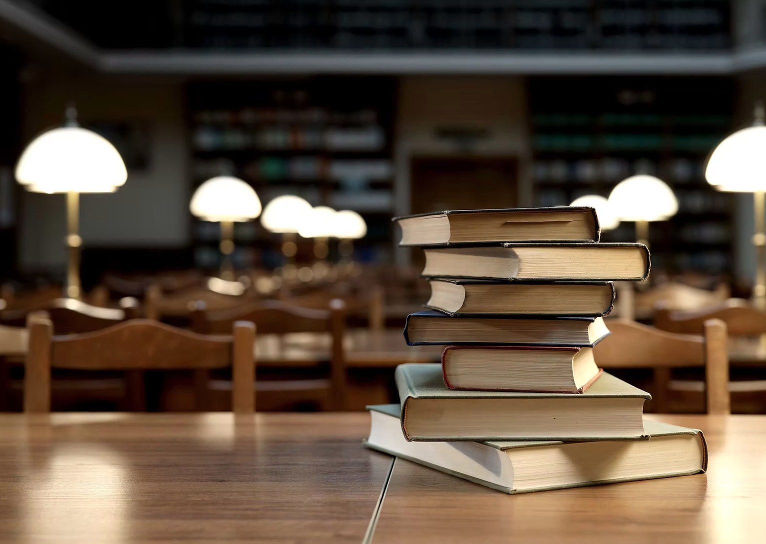 A pile of books rest atop of each other in a grand, traditional looking, wood-heavy library