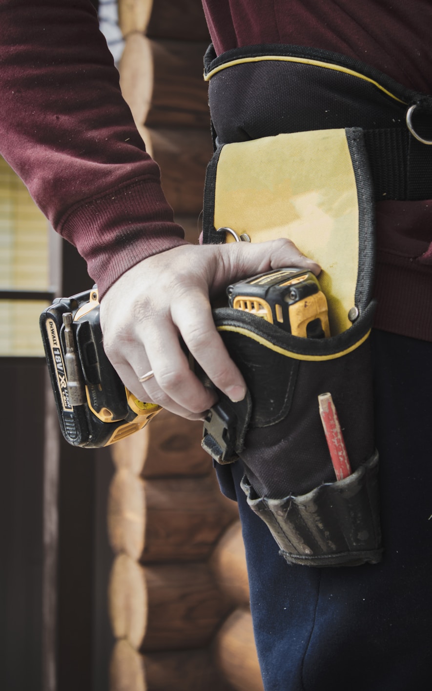 A white male hand that wears a wedding ring rests on a tool in a tool belt