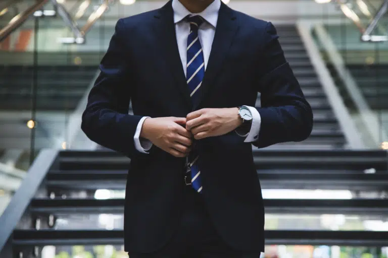 A business man walks down the stairs of a large office and does his navy suit jacket button up.