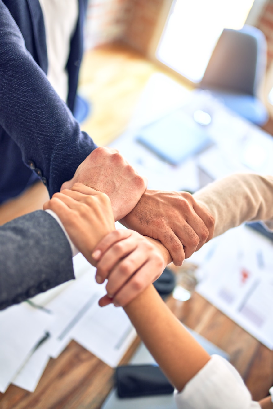 A close up shot of 4 colleagues hands holding a different wrist to create an almost square shape that's connected with their hands