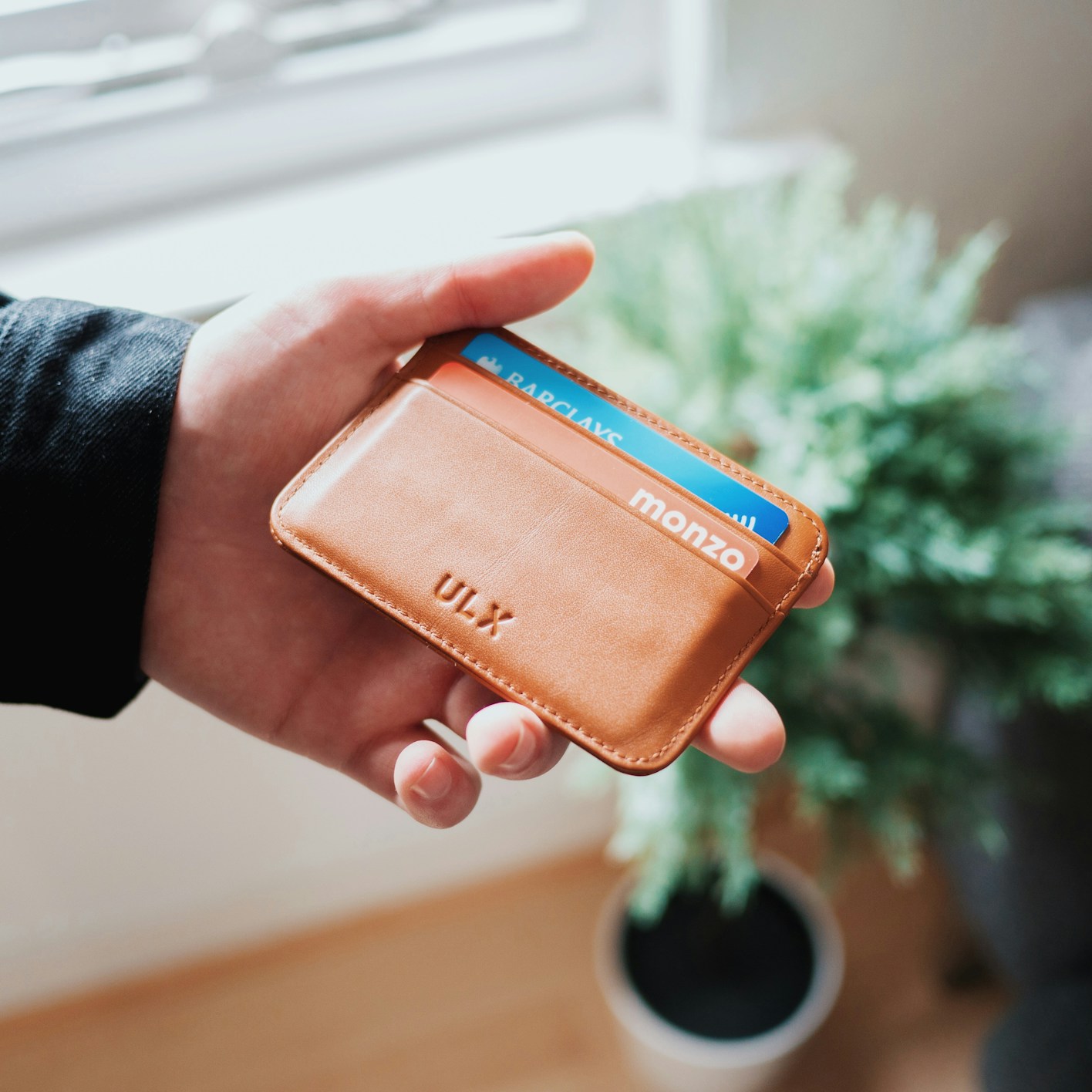 A white hand holds an orange card holder engraved with the initials ULX