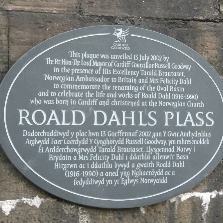 Roald Dahl's Plass in Cardiff, Wales. The oval plaque sits under a footbridge and states that the plass (a Norwegian word for "square") was opened on July 13, 2002 by the Rt Hon. Lord Mayor of Cardiff Councillor Russell Goodway. This is written in English and Welsh.