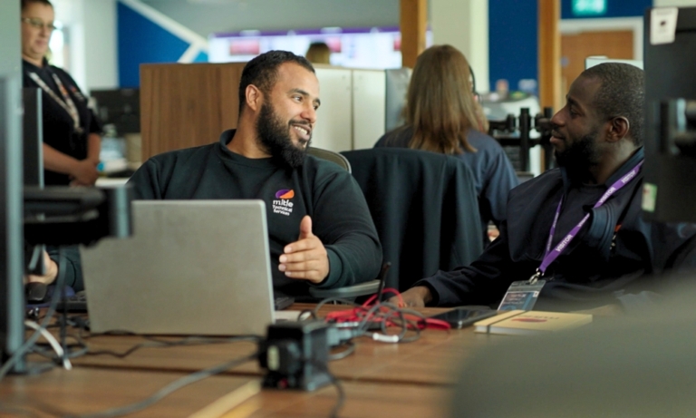 TwoMitie workers sat having a conversation at their desks
