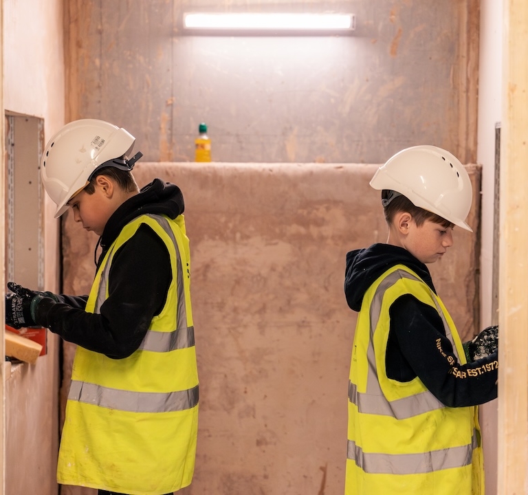 Two learners back to back facing separate walls, concentrating on tiling project