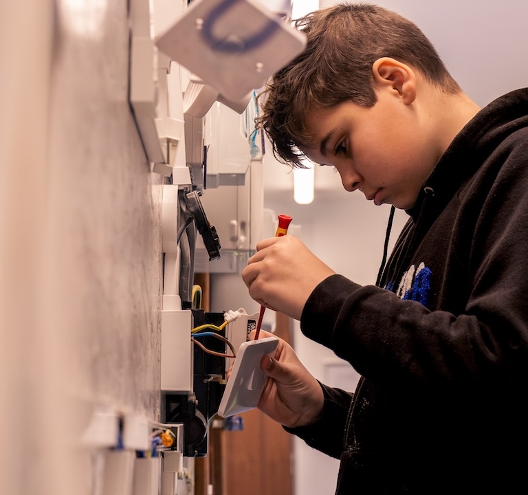 A learner screwing an outlet on an electrical wall