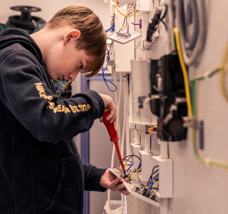 A learner screwing an outlet on an electrical wall