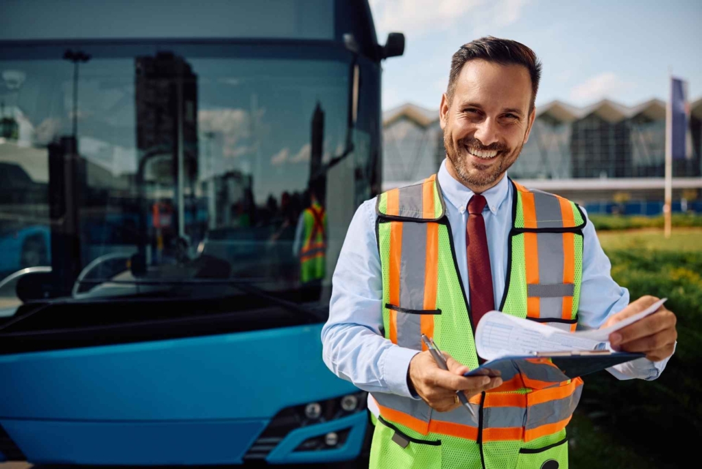 Person in a high-visibility vest holding a clipboard beside a bus.